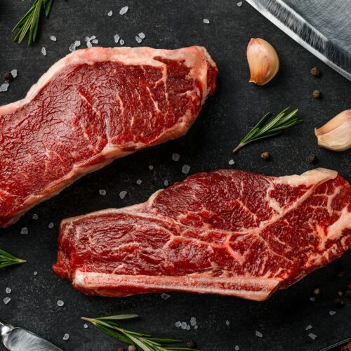 two steaks on a cutting board next to garlic, garlic, and a knife